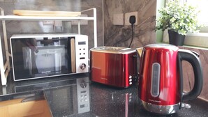 Une cuisine équipée d’un four à micro-ondes, d’un grille-pain et d’une bouilloire électrique rouge, le tout posé sur un plan de travail noir.