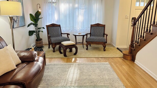 Ein Wohnzimmer mit einem braunen Ledersofa, zwei gemusterten Sesseln, einem kleinen runden Tisch und einer Stehlampe.