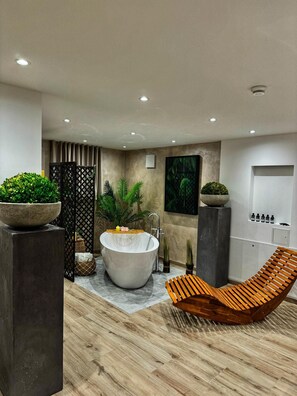 Une salle de bain moderne avec une baignoire sur pieds, un fauteuil de relaxation en bois et diverses plantes.