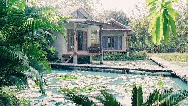 Een huis met een zwembad, omgeven door waterlelies, een houten terras en weelderige begroeiing.