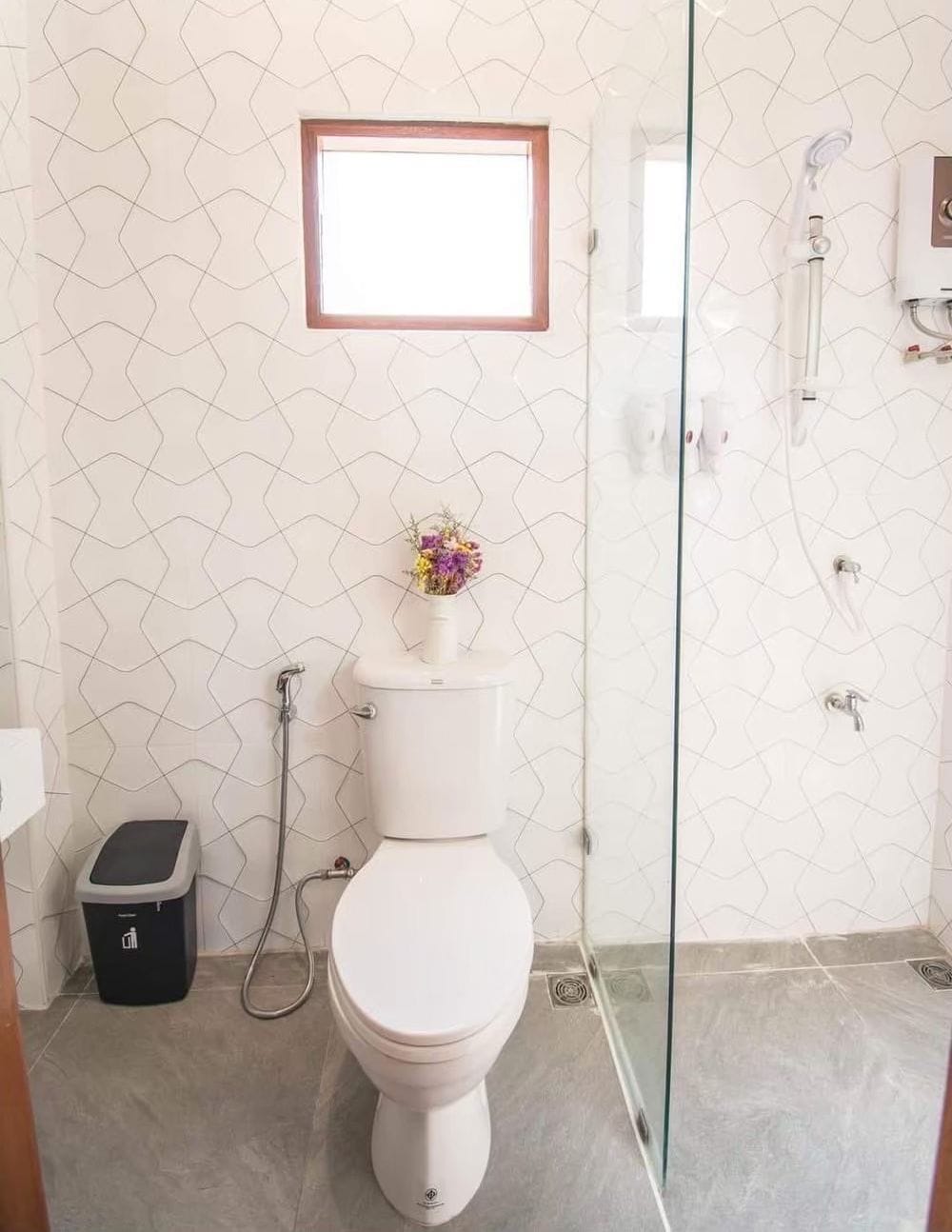 A bathroom with a toilet, a glass shower enclosure, and a small window above the toilet.