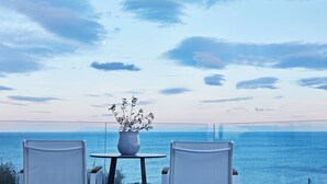 A balcony with two white chairs, a small table, and a potted plant. The view includes a body of water and a clear sky. - Villa Mare ,  this brand new stylish villa boasts spectacular sea views! (Skala)
