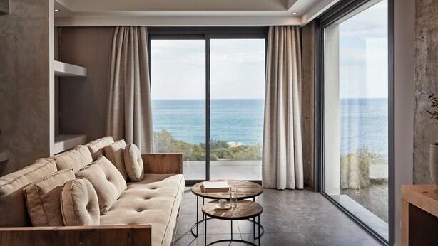A modern living room with a large window overlooking the sea, a sofa, a small round table, and a bookshelf. - Villa Mare ,  this brand new stylish villa boasts spectacular sea views! (Skala)