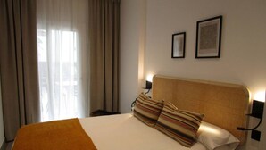 A hotel room with a bed, a window with curtains, and two framed pictures on the wall. - Travel Habitat Ruzafa Green House Patio (València)