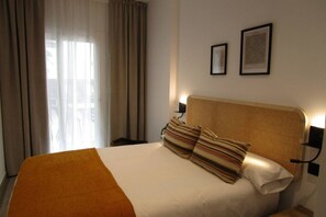 A hotel room with a bed, a window with curtains, and two framed pictures on the wall.