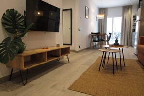 Ein modernes Wohnzimmer mit einer Holzeinrichtungsanlage, einem an der Wand montierten Fernseher, einem Essbereich mit Tisch und Stühlen und einer großen Pflanze.