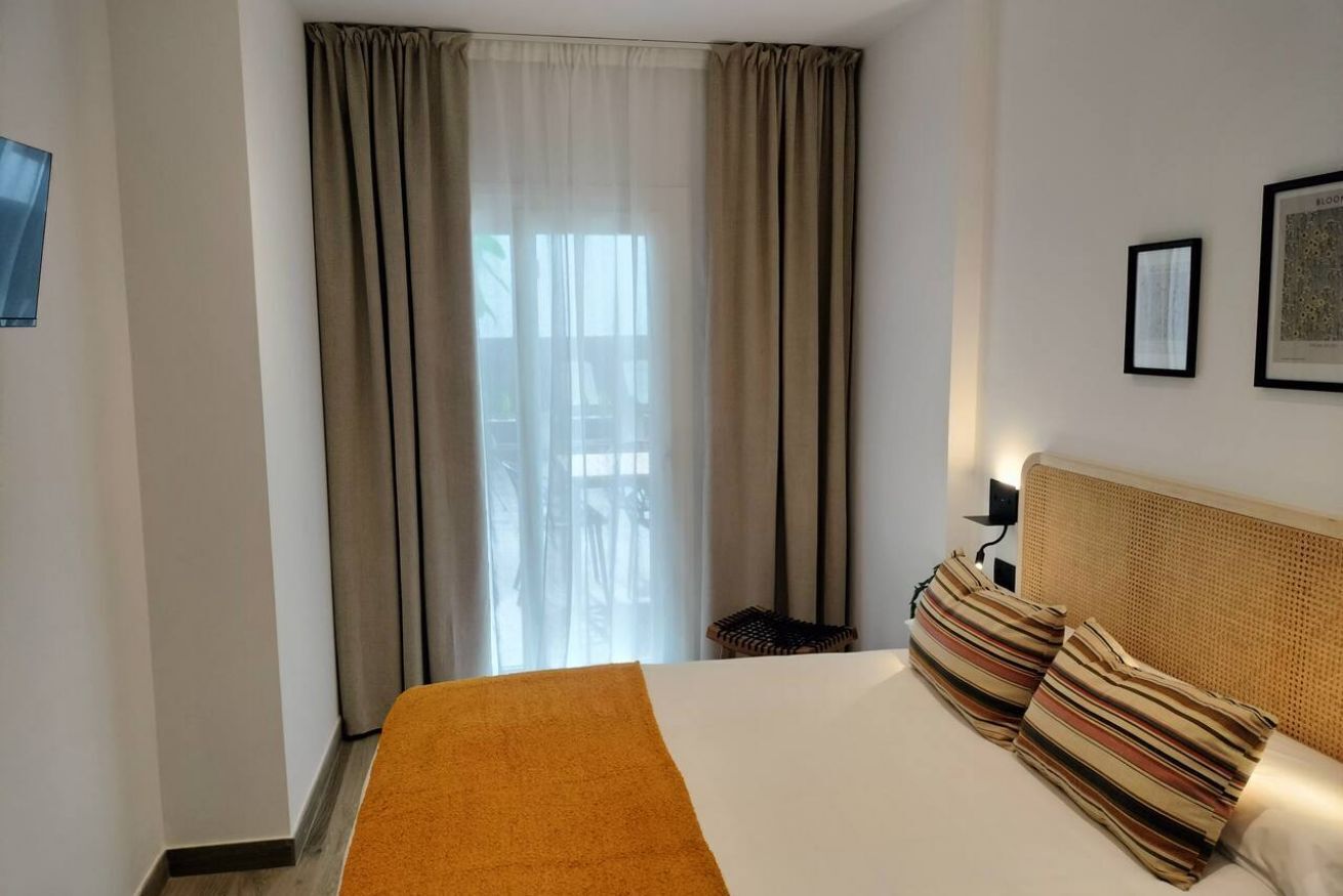 Une chambre d’hôtel avec un grand lit, une tête de lit, une fenêtre avec des rideaux et une lampe fixée au mur.