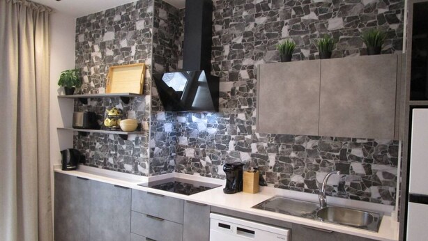 A modern kitchen with a stone backsplash, built-in appliances, and grey cabinetry. - Travel Habitat Ruzafa Green House Patio (València)