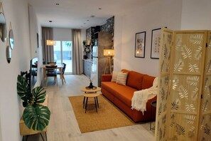 A modern living room with a sofa, a dining table, and a kitchen area in the background.