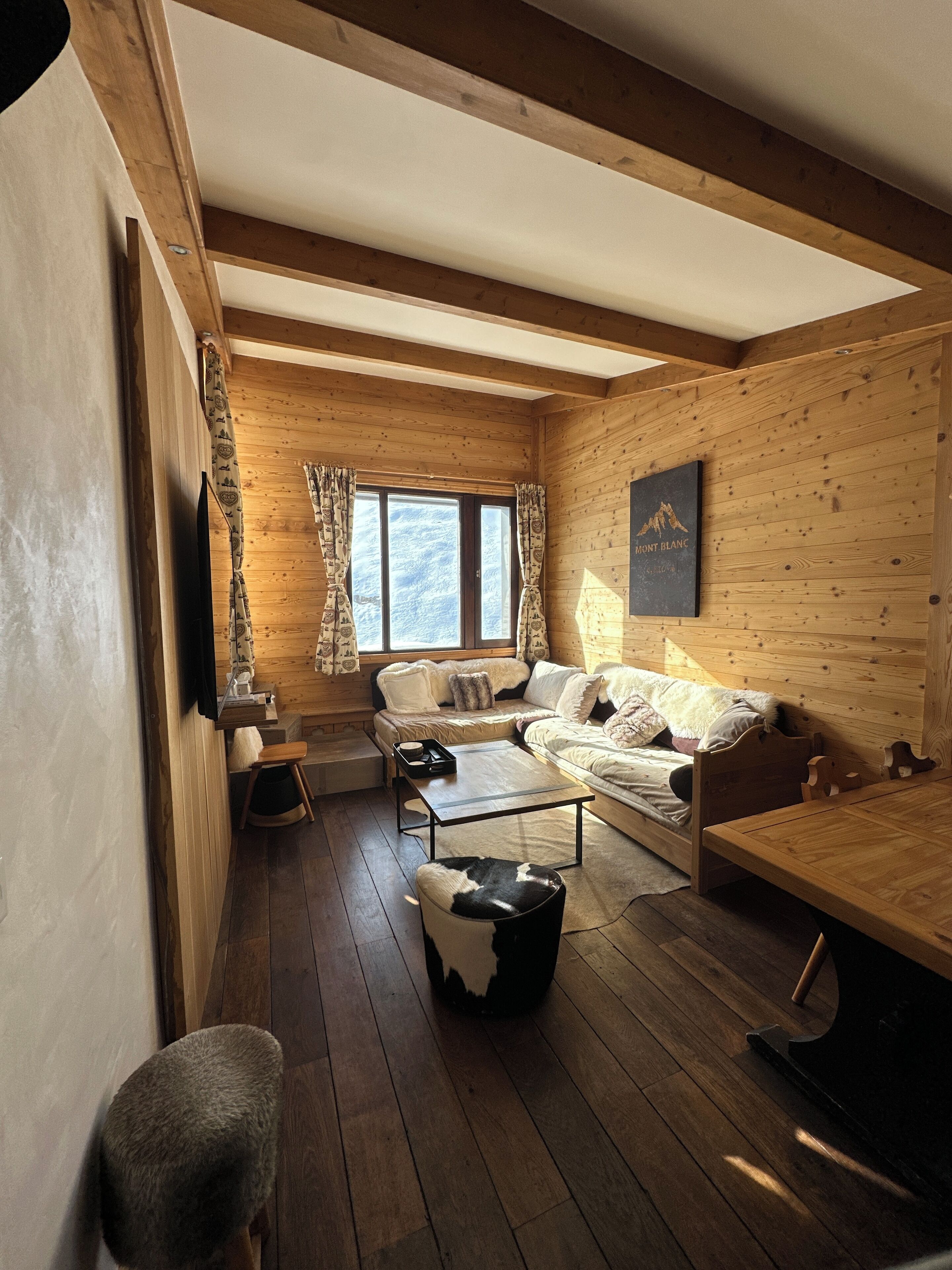 Een gezellig cabin-interieur met houten wanden, een bank, een eettafel en een raam met gordijnen.