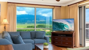 Una sala de estar con un ventanal grande, un sofá, un televisor y una mesita con una planta.