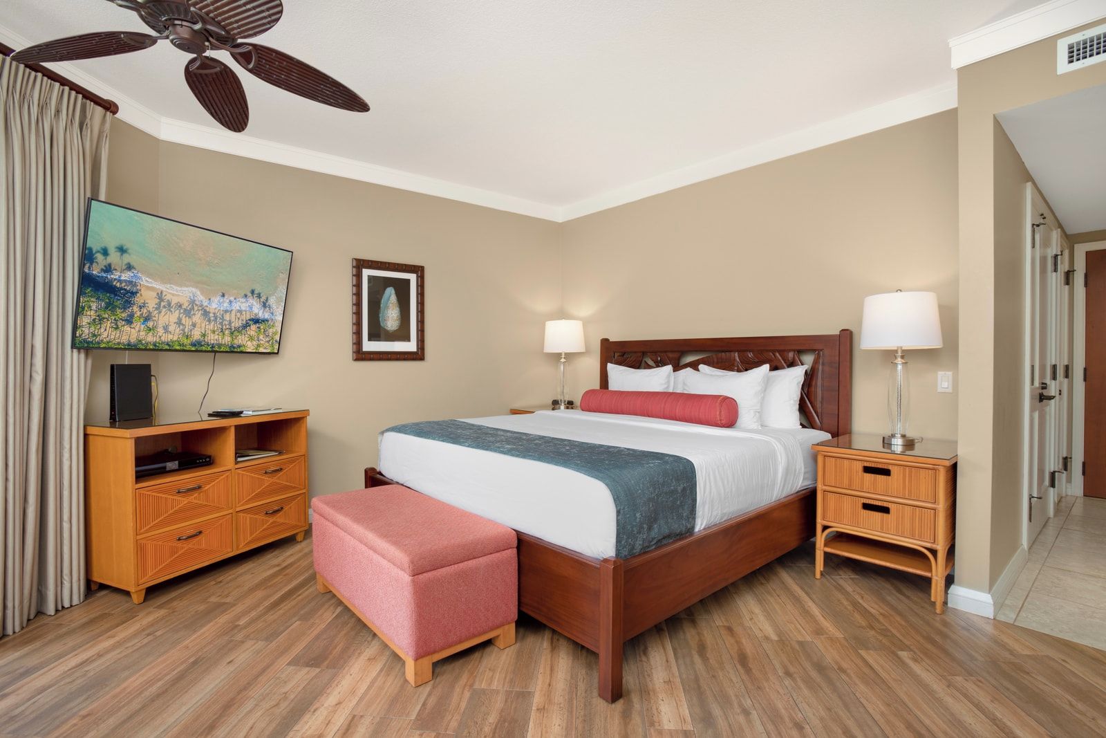 A hotel room with a bed, wooden nightstands, a TV, a ceiling fan, and a painting on the wall.