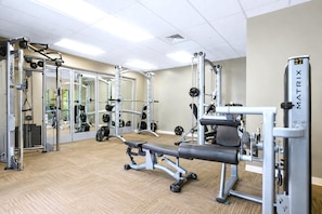 Ein Fitnessstudio mit verschiedenen Trainingsgeräten, darunter eine Hantelbank, Kraftgeräte und Kurzhanteln.