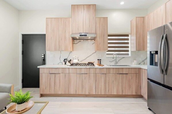 A modern kitchen with wooden cabinets, a stainless steel refrigerator, and a built-in stove. - Cozy Modern Home w Full Kitchen & Parking (Baldwin Park)