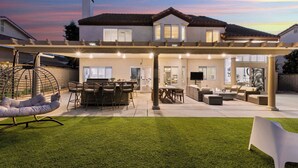 Ein zweigeschossiges Haus mit überdachter Terrasse, ausgestattet mit Gartenmöbeln und einem Schaukelstuhl.