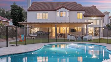 A residential property with a swimming pool, a covered patio with outdoor furniture, and a well-maintained lawn.