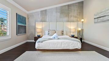 A bedroom with a large bed, two bedside tables, a floor lamp, and a window with blinds.