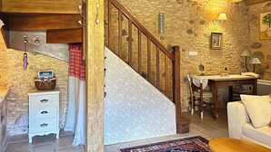 A rustic interior with a wooden staircase, stone walls, a dining area with a table and chairs, and a white sofa. - Gîte for 2 people with swimming pool - In the heart of Périgord noir (Saint-Cyprien)