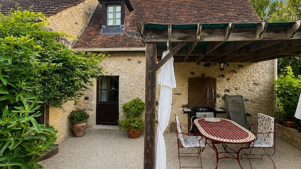 A stone house with a tiled roof, a wooden pergola, a table with chairs, and potted plants. - Gîte for 2 people with swimming pool - In the heart of Périgord noir (Saint-Cyprien)