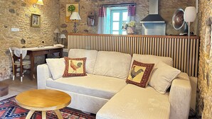 A cozy living room with a stone wall, a sofa with decorative pillows, a wooden table, and a window with curtains. - Gîte for 2 people with swimming pool - In the heart of Périgord noir (Saint-Cyprien)