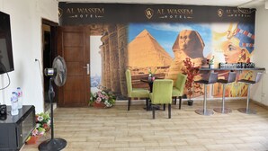 A hotel reception area with a large mural of the pyramids, green chairs, a fan, and a water dispenser. - lora Altahrir hotel (Cairo)