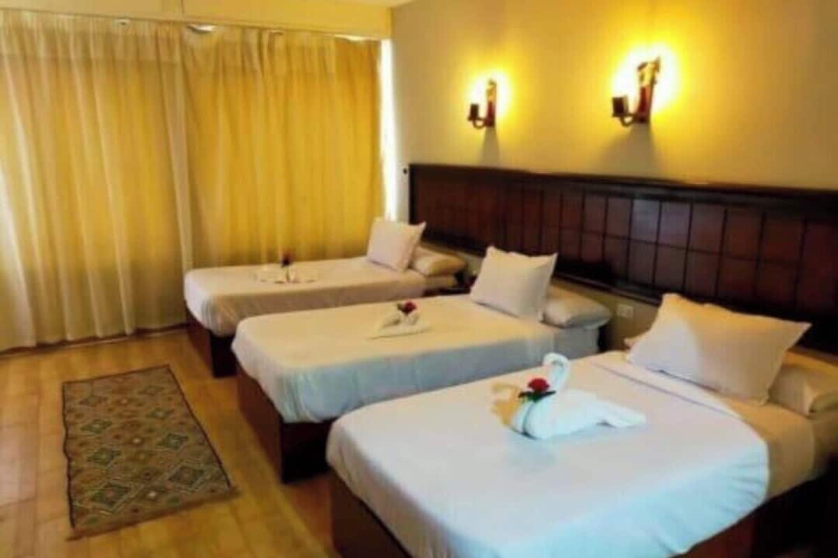 A hotel room with two single beds, a wooden floor, a beige curtain, and two wall-mounted lights.