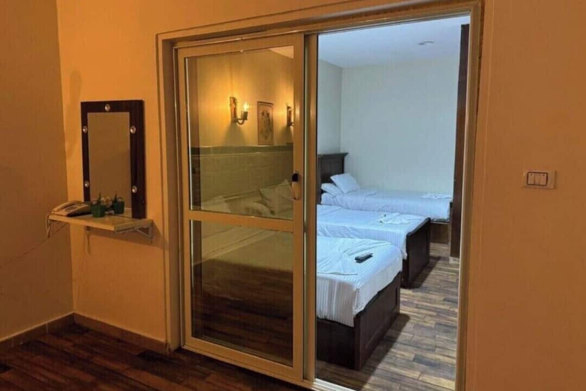 A hotel room with a sliding glass door leading to a balcony, a bedside table with a phone, and two beds with white bedding.