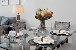 A dining table set for four with clear glassware, a vase with flowers, and wicker chairs.