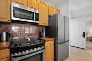 A kitchen with a stainless steel oven, microwave, and refrigerator, wooden cabinets, and a granite countertop.