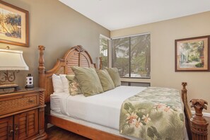 Een slaapkamer met een houten bed, een nachtkastje, een lamp en een raam met jaloezieën.