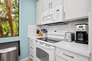 A kitchen with white cabinets, a microwave, a toaster, a coffee maker, and a stove. - Grand Champions | Ocean View 2 BR, Sleeps 8 | Car Incl. w/ 6+ Nights | GCH ML-1493 by KBM (Wailea)