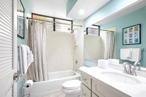 Une salle de bain équipée d’une baignoire, de toilettes et d’un lavabo, avec un mur orné d’un motif à carreaux et un grand miroir.