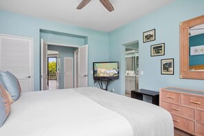 Ein Schlafzimmer mit einem Bett, einem Fernseher, einem Schminktisch und einer Tür, die auf einen Balkon führt.