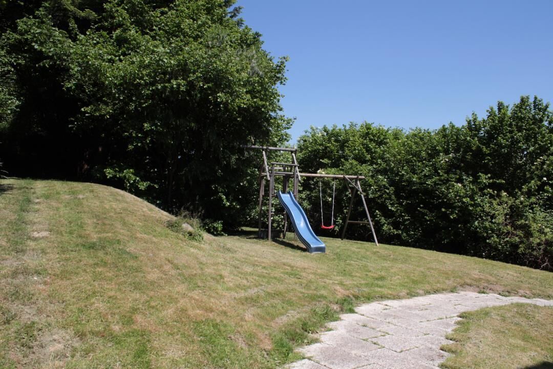A playground with a slide and swings set on a grassy hill.