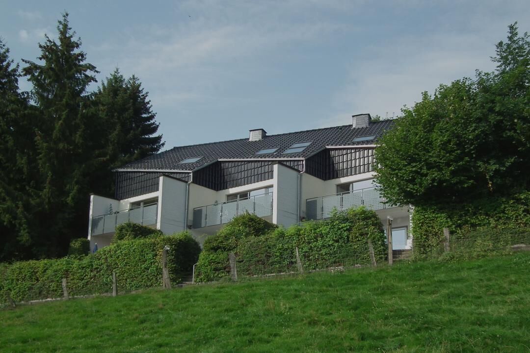 Une maison moderne à deux étages, dotée d’un toit en pente, de grandes fenêtres et d’une pelouse devant.