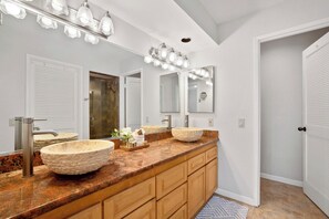 Un baño con tocador doble, dos lavamanos tipo recipiente, un espejo grande con luces y armarios de madera.