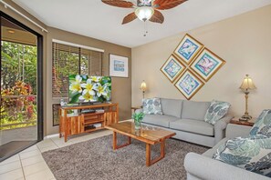 Una sala de estar con televisor, sofá, mesa de centro y almohadones decorativos.