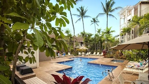 A pool area with lounge chairs and a small pool, surrounded by palm trees and greenery.