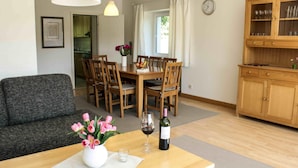 Un coin repas avec une table en bois, des chaises, un vase de fleurs et une bouteille de vin.