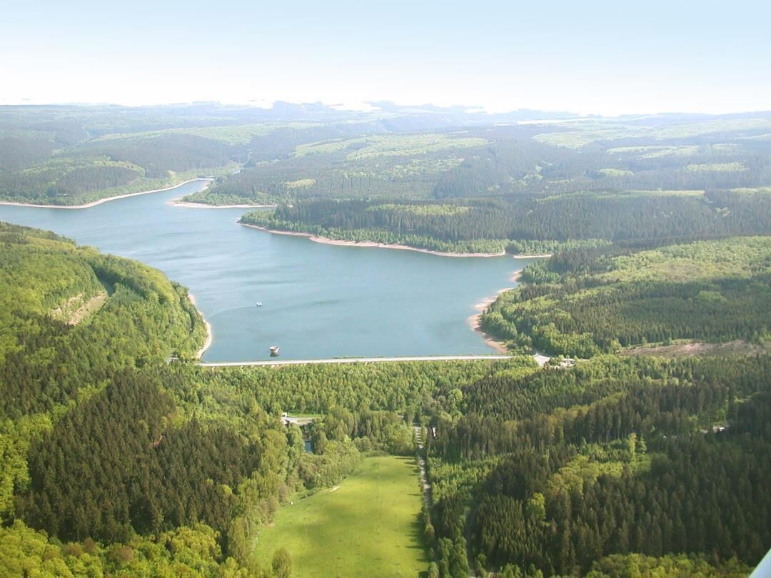 Vista aérea de un lago rodeado de bosques densos y un edificio pequeño cerca de la orilla.