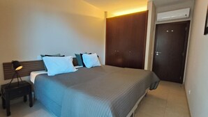 A hotel room with a bed, bedside table, lamp, wardrobe, and an air conditioning unit. - Oasis by Templesuites (Portimão)