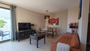 A modern living room with a sofa, TV, dining table, and chairs. - Oasis by Templesuites (Portimão)