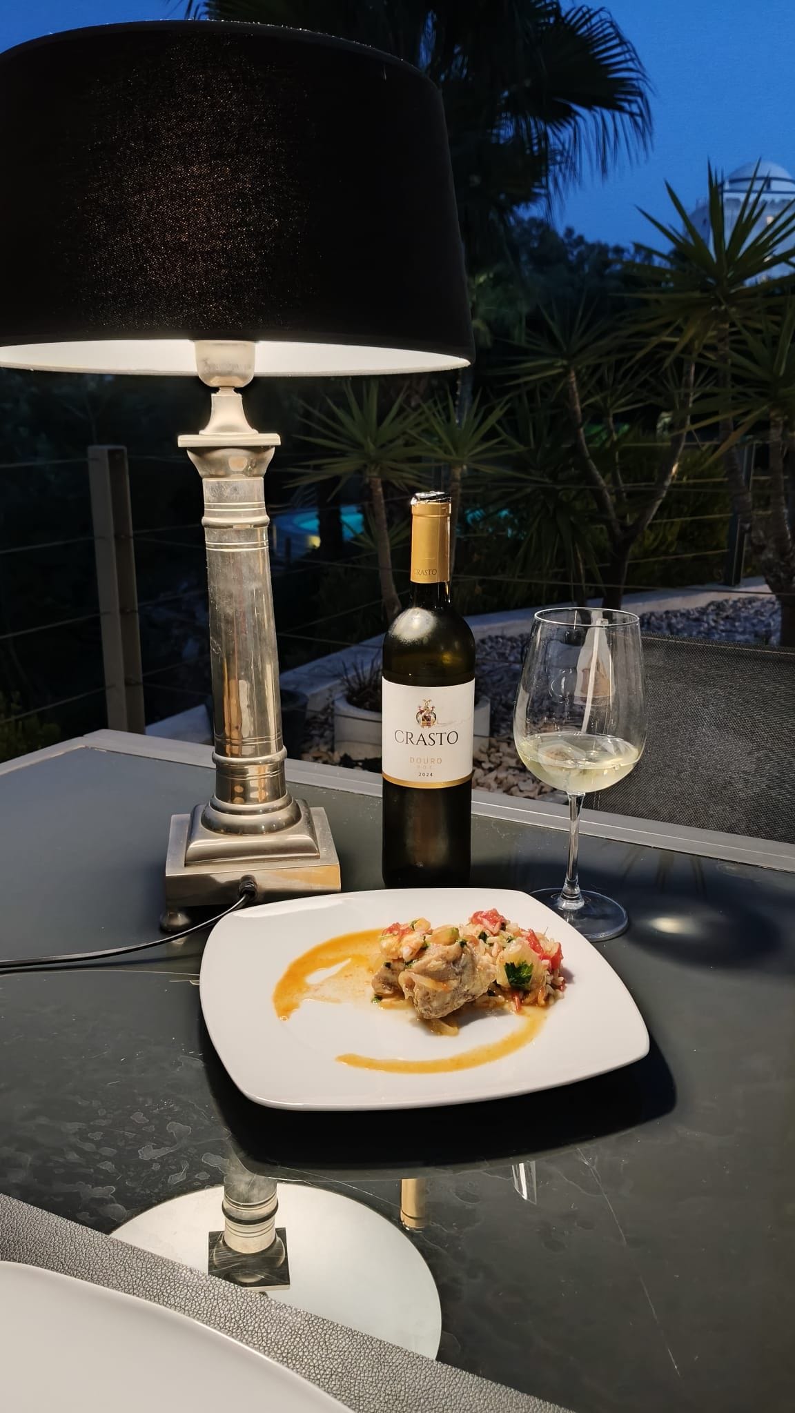 A table with a bottle of Crasto Douro wine, a glass of white wine, and a plate of food.