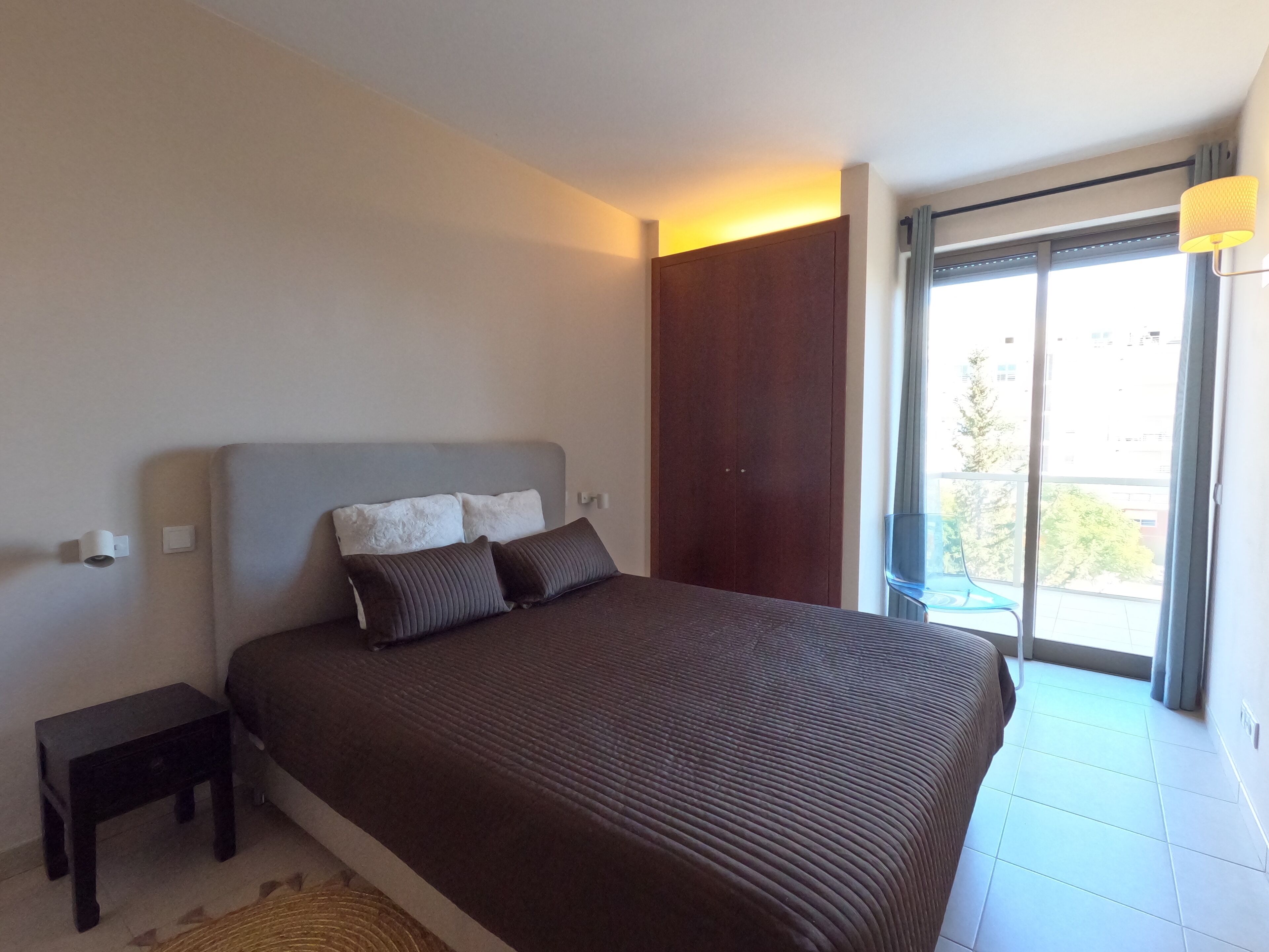 Een slaapkamer met een groot bed, een nachtkastje, een kledingkast en een balkon met uitzicht.
