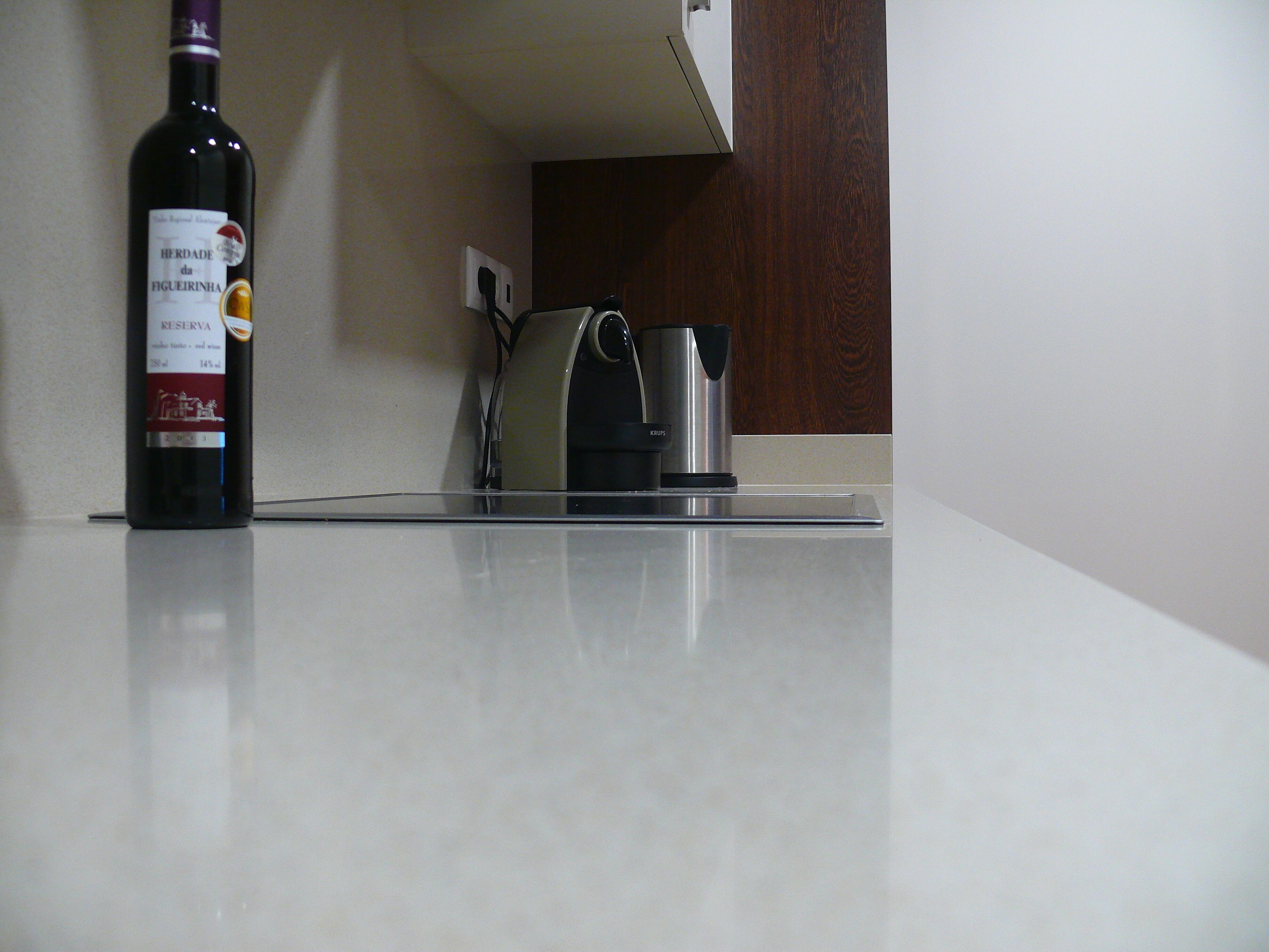 Une bouteille de vin posée sur un comptoir, avec une machine à café et une prise électrique en arrière-plan.