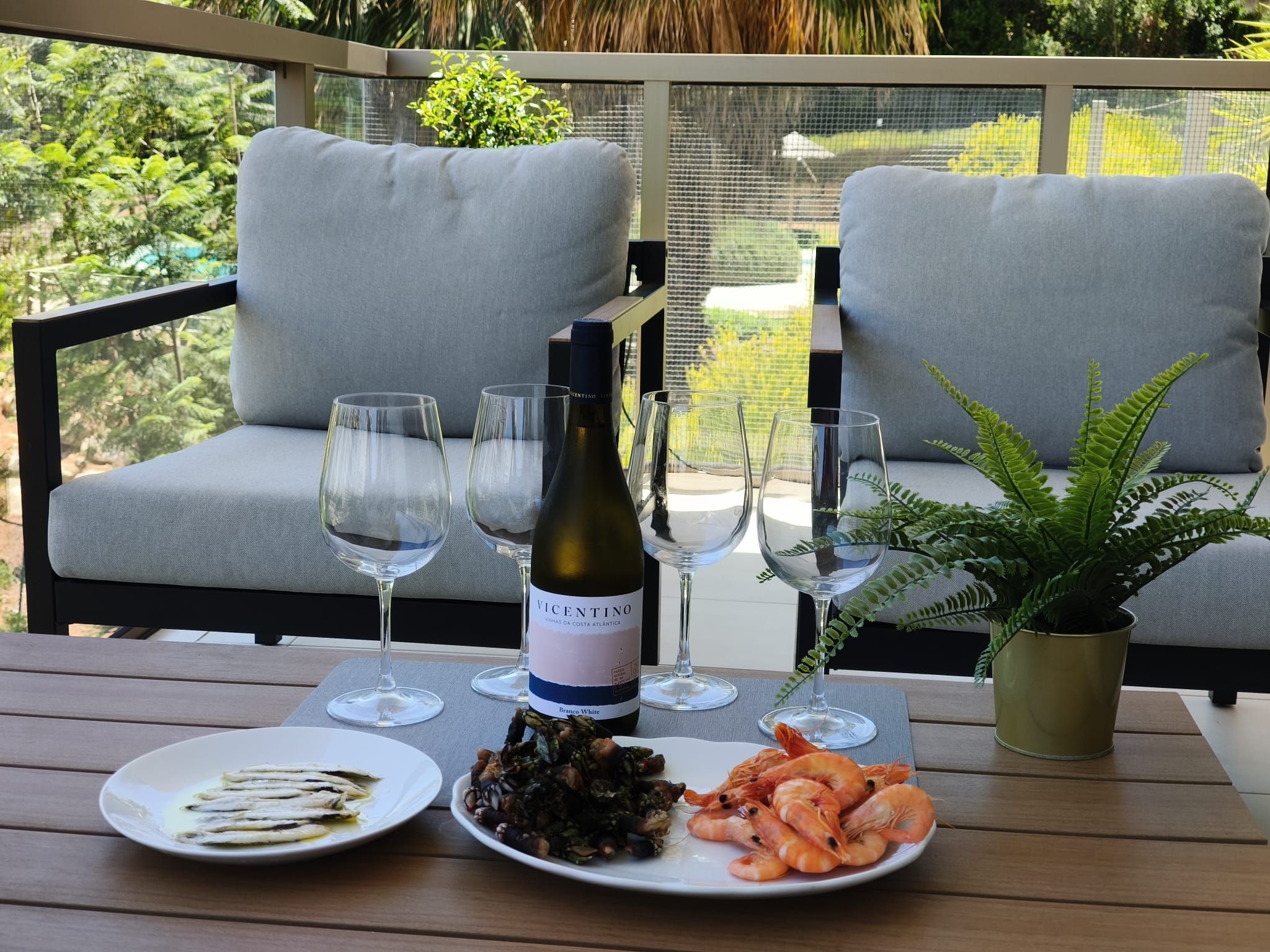 Une table à manger avec une bouteille de vin, des verres, des assiettes de fruits de mer et une plante de fougère.