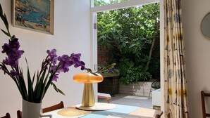 A dining area with a table set for two, a vase of purple flowers, a lamp, and a painting on the wall. - St Martins Walk - Three Bedroom Apartment, Sleeps 6 (York)
