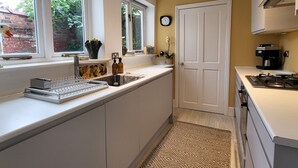 A compact kitchen with white cabinets, a built-in sink, a stove, and a window with a view of greenery outside. - St Martins Walk - Three Bedroom Apartment, Sleeps 6 (York)
