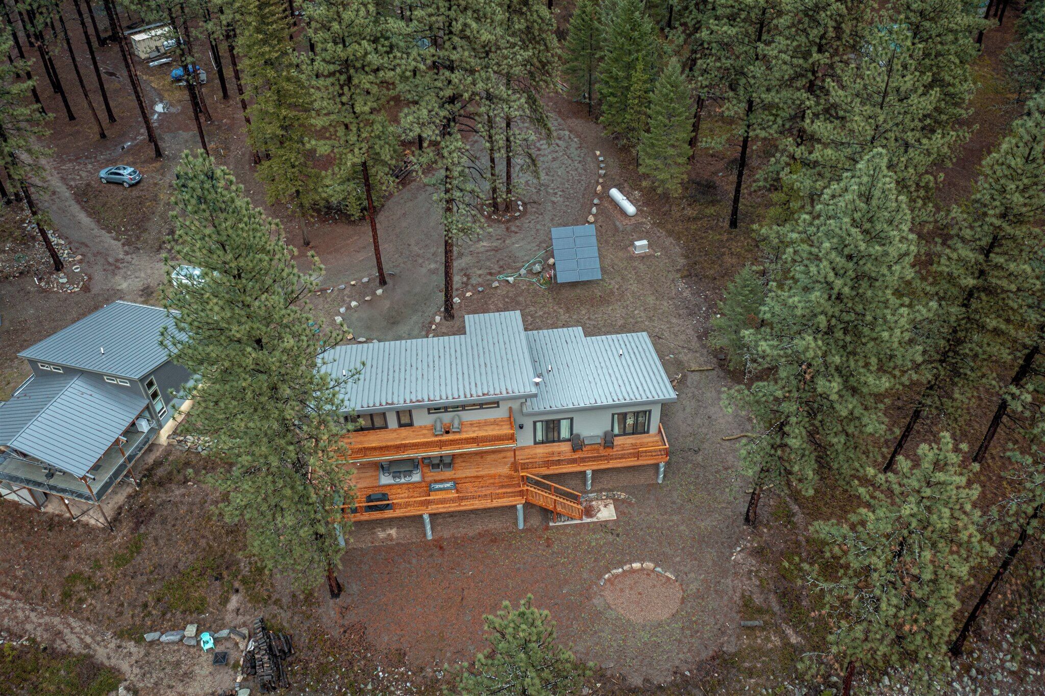 A two-story house with a deck, surrounded by a forest.