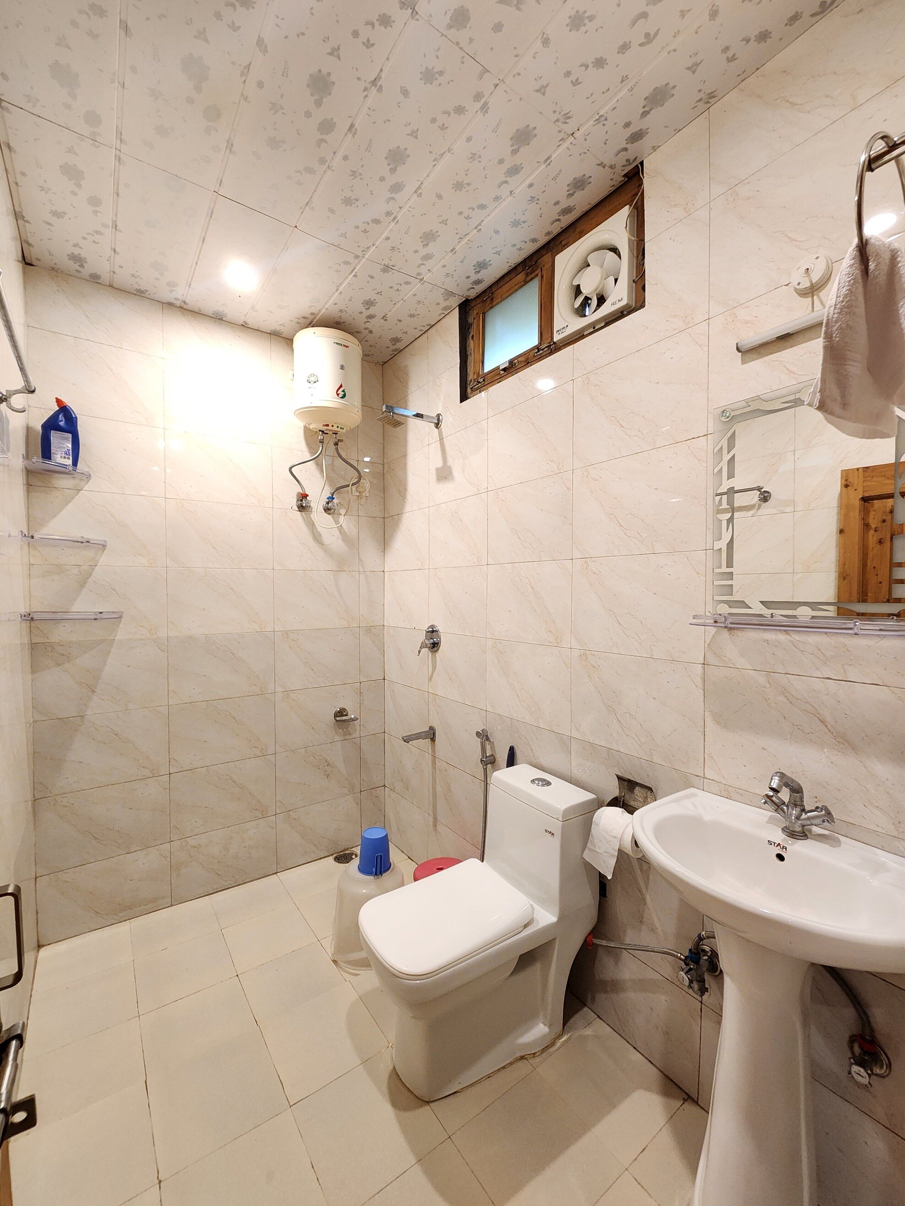 A bathroom with a toilet, sink, shower, and a mirror.